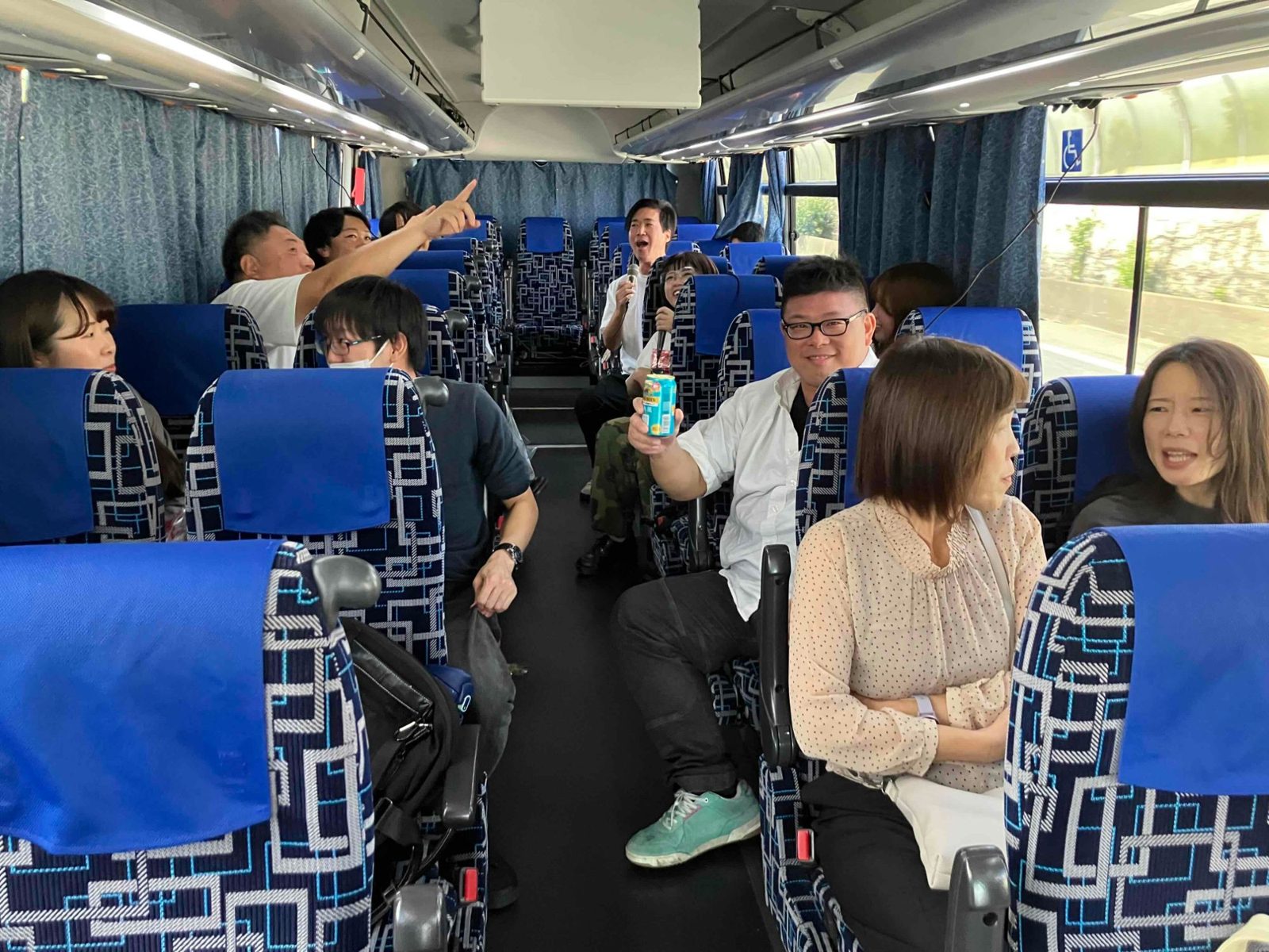 貸し切りバスの車内で、マイクを手にカラオケを楽しむタックス・プラン税理士法人の社員たち